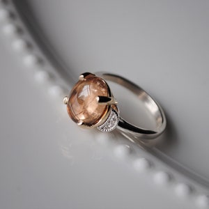 May include: A ring with a large, round, brown gemstone set in a gold claw setting. The band is silver and has a small row of clear gemstones on one side.
