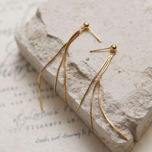 Peut inclure: Une paire de boucles d'oreilles dorées dotées d'un petit clou à bille et de trois chaînes serpent souples et délicates qui pendent vers le bas. Les boucles d'oreilles présentent une finition polie et un design fin et allongé pour un mouvement fluide.