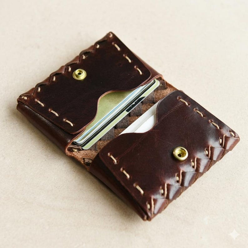 May include: Open brown leather card holder with a brass snap closure. The card holder is hand-stitched with a decorative edge and contains several cards. The leather has a rich, textured appearance.