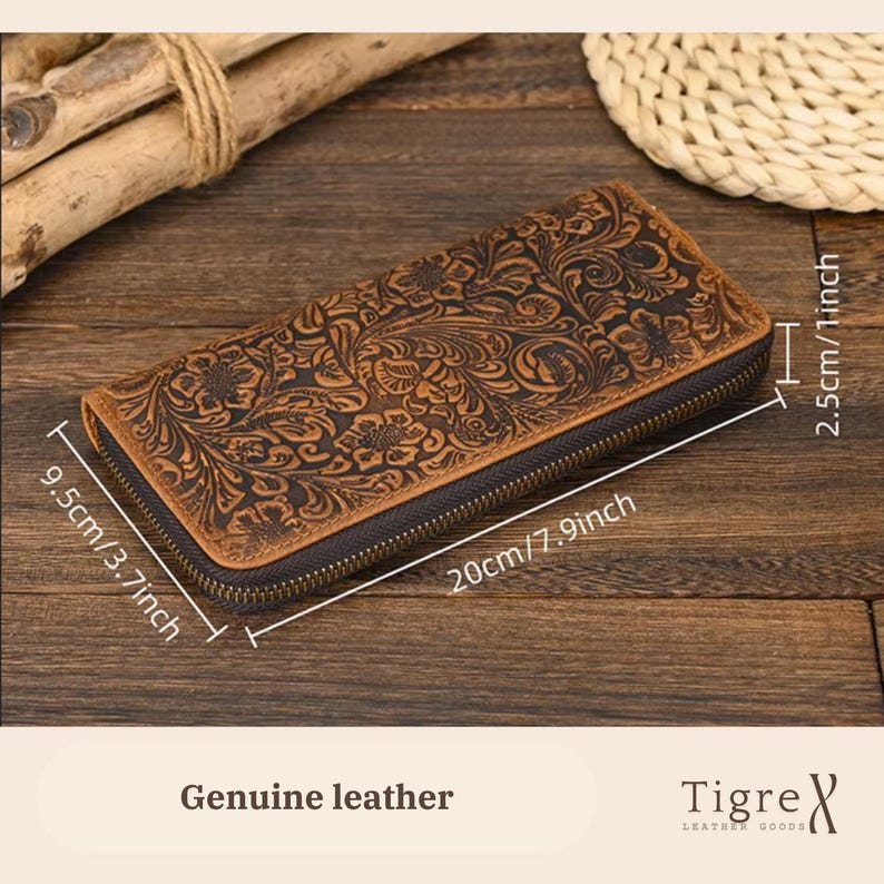 Op de afbeelding: Een bruine lederen portemonnee met een ingewikkeld bloemenpatroon in reli&euml;f en een donkere ritssluiting. De portemonnee is 20 cm lang, 9,5 cm breed en 2,5 cm hoog. De tekst "Genuine leather" en "Tigre" zijn zichtbaar op de afbeelding.