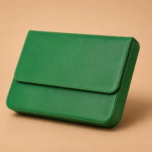Pode incluir: Uma clutch retangular verde esmeralda com fecho de aba. A bolsa &eacute; feita de um material liso e apresenta uma borda costurada. A clutch est&aacute; sobre um fundo neutro.