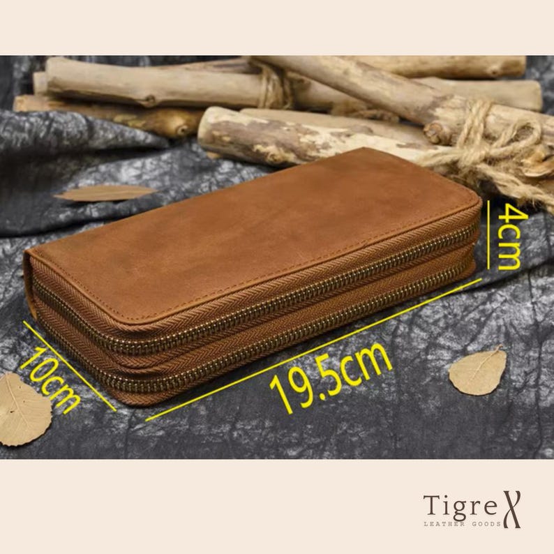 Op de afbeelding: Een rechthoekig bruin lederen etui met twee compartimenten met ritssluiting. Het etui is 19,5 cm lang, 10 cm breed en 4 cm hoog. De buitenkant heeft een gladde, matte afwerking met metalen ritsen die langs de zijkanten lopen.