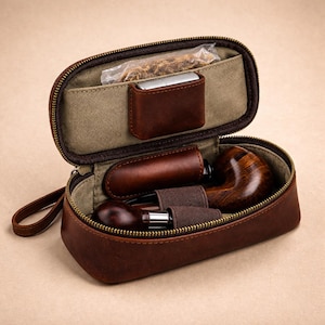 May include: A brown leather pipe case with a zipper, containing a tobacco pipe, tobacco, and a lighter. The case has a canvas lining and a small leather pocket. The pipe is made of wood and metal.
