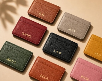 Op de afbeelding: Een verzameling gepersonaliseerde leren kaarthouders in verschillende kleuren, waaronder bruin, rood, groen, zwart, oranje, grijs, geel en roze. Elke kaarthouder heeft goudkleurige letters met namen of initialen.