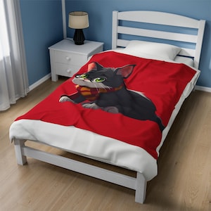 May include: Red fleece blanket featuring a black and white cat wearing glasses and a yellow and red scarf. The cat is looking to the left.