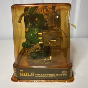 May include: The Incredible Hulk Collectors Clock with working lights, in a clear plastic display case. The clock features a green Hulk figurine and a gold-colored clock mechanism. The packaging has the Marvel logo.