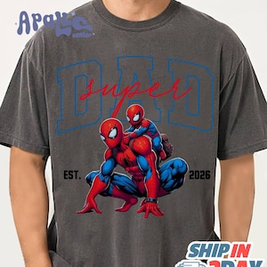 A gray t-shirt with a graphic design featuring two Spider-Man characters, one larger and one smaller, with the text "SUPER DAD" and "EST. 2026" printed on it.