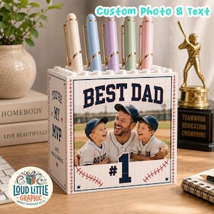 May include: A white rectangular desk organizer with a brick-like texture, featuring a custom photo of a man and two children in baseball uniforms. The text reads BEST DAD, #1, and YOU'RE MY MVP, LOVE, MAX & CHARLIE. Five pastel pens sit in the top slots.