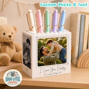 May include: A white block-style pen holder featuring a custom photo of a father and child, with the printed text I Love You Daddy and Love, Noah. The holder contains five pastel-colored pens in cream, pink, mint green, lavender, and light blue.