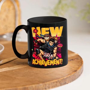 May include: Black ceramic mug featuring a colorful graphic of a cartoon character with a furry sidekick, a donut, and the words "NEW ACHIEVEMENT!" The mug has a black handle and a glossy finish. The design is set against a red and pink background.