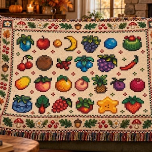May include: A woven throw blanket featuring a cream-colored center with a grid of pixelated fruit, vegetable, and nature icons. The border displays a repeating pattern of red berries, green oak leaves, acorns, and white flowers.