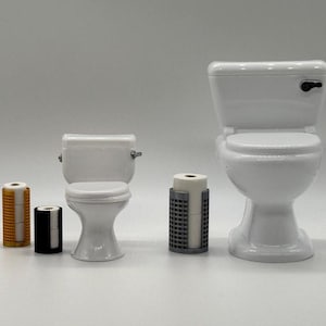 May include: A set of four miniature bathroom accessories, including a white toilet, a white toilet seat, a black toilet paper holder, a gold toilet paper holder, and a gray toilet paper holder with a roll of toilet paper.
