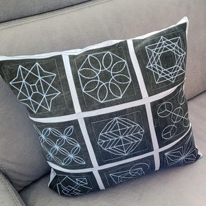May include: A black and white geometric patterned throw pillow with a white background and black geometric designs. The pillow is on a gray couch.