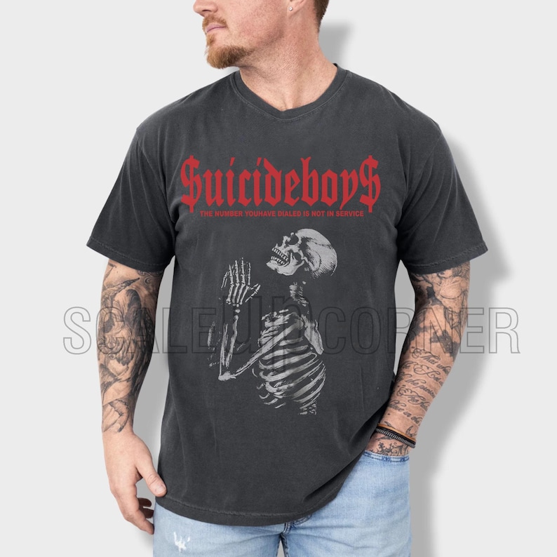 May include: Dark gray t-shirt featuring the text "Suicideboys" in red gothic font above a detailed illustration of a praying skeleton. The text "The number you have dialed is not in service" is below the main text.