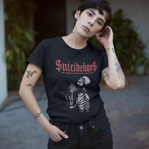 May include: Black t-shirt with the text "Suicideboys$" in red gothic lettering above a white illustration of a skeleton. The phrase "THE NUMBER YOU HATE RULES IS NOT IN ARROWE" is below the main text.