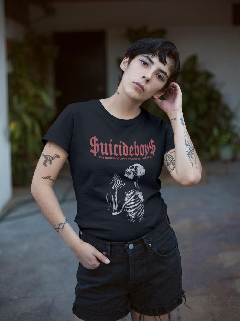 May include: Black t-shirt with the text "Suicideboys$" in red gothic lettering above a white illustration of a skeleton. The phrase "THE NUMBER YOU HATE RULES IS NOT IN ARROWE" is below the main text.