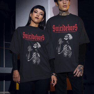 May include: Black t-shirts with the text "Suicideboys" in red gothic font. The shirts feature a skeleton graphic with praying hands. The phrase "THE NUMBER YOU HAVE DIALED IS NOT IN SERVICE" is printed below the logo.