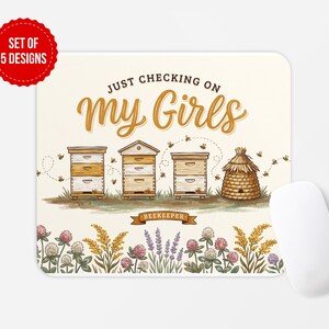 以下が含まれることがあります： クリーム色の背景に「JUST CHECKING ON My Girls」とバナーに「BEEKEEPER」の文字が書かれた長方形のマウスパッド。イラストには3つの木製巣箱、藁製の巣箱、飛んでいるミツバチ、そして手前にクローバーとラベンダーの花が描かれています。