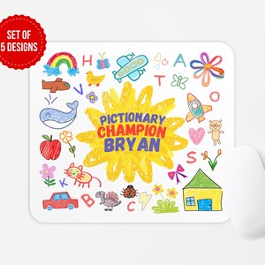 May include: A white mouse mat featuring colourful, childlike drawings of a rainbow, whale, apple, and other objects. The mouse mat has the text "PICTIONARY CHAMPION BRYAN" in the centre, surrounded by a yellow sunburst design. A white computer mouse is on the right.