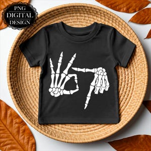 Pode incluir: Camiseta preta com um gráfico de mão de esqueleto branco fazendo o gesto de 'ok'. A camiseta também tem o texto "PNG DIGITAL DESIGN" em um design circular. Perfeita para o Halloween ou eventos temáticos.