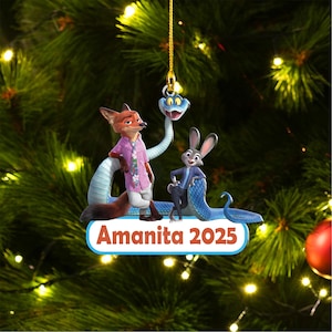 May include: A Christmas ornament featuring cartoon characters Nick Wilde, Judy Hopps, and a snake. Nick is wearing a pink shirt and white pants. Judy is in a blue suit. The ornament has the text "Amanita 2025".