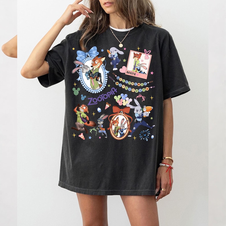 May include: Black t-shirt featuring colorful cartoon characters from Zootopia. The design includes images of a fox and a rabbit, along with the word "Zootopia" and the word "Bestie". The shirt has a relaxed fit.