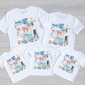 Peut inclure: Cinq t-shirts blancs &agrave; manches courtes avec un motif color&eacute; repr&eacute;sentant une sir&egrave;ne, un prince et des cr&eacute;atures marines c&eacute;l&eacute;brant un deuxi&egrave;me anniversaire. Chaque t-shirt porte le texte Daddy, Mommy, Brother, Sister ou Birthday Girl avec un deux.