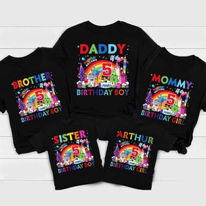 May include: Black t-shirts with colorful birthday-themed graphics. The shirts feature the number 5, rainbows, and the words "Daddy," "Mommy," "Brother," "Sister," and "Arthur," along with "Birthday Boy" and "Birthday Girl."
