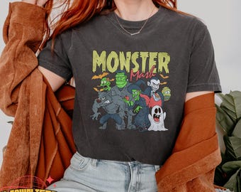 May include: Dark grey t-shirt with a cartoon graphic of monsters such as a werewolf, Frankenstein's monster, a witch, and a vampire. The text "Monster Mash" is printed above the characters in green and yellow.