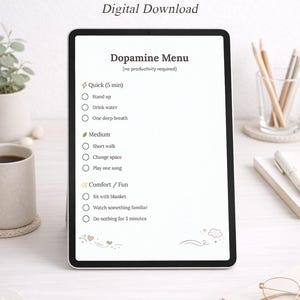 Op de afbeelding: Een digitale planner voor ADHD, met een "Dopamine Menu" met snelle, gemiddelde en comfort/leuke activiteiten. De tablet staat op een wit oppervlak met een kopje, potloden en een bril.