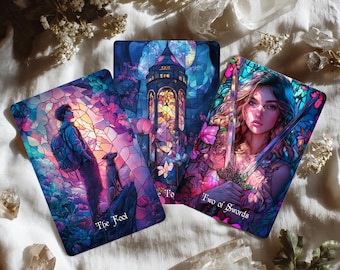 May include: Three tarot cards with colorful illustrations. The cards feature images of a person with a dog, a tower, and a woman holding swords. The cards are surrounded by crystals and flowers on a white surface.