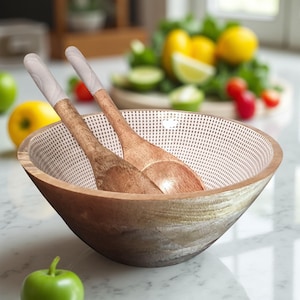 Può includere: Una ciotola per insalata in legno con due cucchiai di legno all'interno. La ciotola ha un motivo a pois bianchi all'interno e una finitura in legno naturale all'esterno. Limoni, lime e pomodori sullo sfondo.