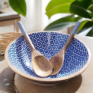 Könnte beinhalten: Eine blaue und weiße gemusterte Salatschüssel aus Holz mit zwei passenden Holz-Servierbesteck.