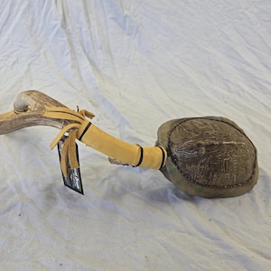 May include: A handcrafted wooden club with a rounded head and a curved handle. The club features tan leather accents and a dark, textured head. The handle is made of a light-colored wood.