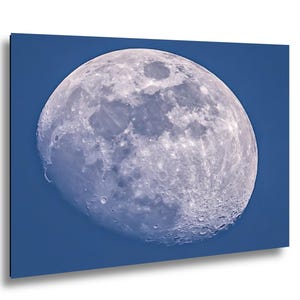 May include: A close-up of the moon against a deep blue sky. The moon is a pale gray color with visible craters and surface details. The image is a print on a rectangular canvas.