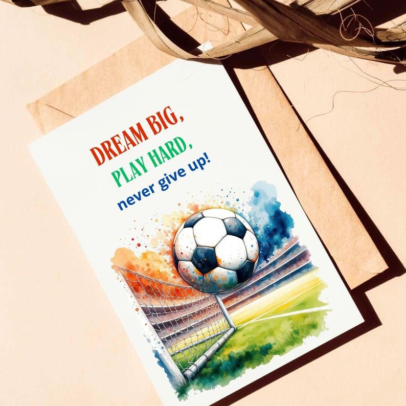 Puede incluir: Una ilustraci&oacute;n de acuarela de un bal&oacute;n de f&uacute;tbol volando hacia una porter&iacute;a. El fondo es una acuarela colorida de un estadio. El texto "DREAM BIG, PLAY HARD, never give up!" est&aacute; escrito en rojo, verde y azul.