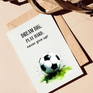 May include: A white card with black text that reads "Dream Big, Play Hard, never give up!" and a watercolor illustration of a soccer ball on green grass.