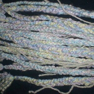 May include: A close-up of a bundle of yarn in shades of blue, purple, and white. The yarn is braided and has a soft, fluffy texture.