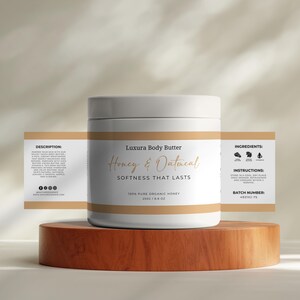 May include: White jar of Luxura Body Butter Honey & Oatmeal, a 100% pure organic honey product. The jar is labeled with the product name, ingredients, instructions, and batch number. The jar is sitting on a wooden surface.