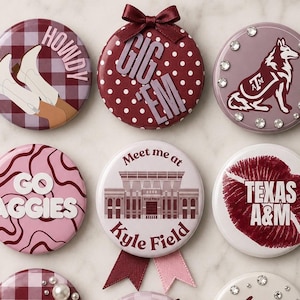 May include: Six circular pin-back buttons featuring Texas A&M themes. Designs include white boots on a maroon plaid background with 'HOWDY', a maroon polka dot button with 'GIG 'EM' and a bow, a maroon dog logo with rhinestones, 'GO AGGIES' on pink swirls, a Kyle Field illustration, and a red lip print with 'TEXAS A&M'.
