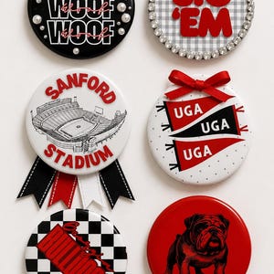 Puede incluir: Seis chapas redondas con varios diseños: una negra con texto blanco WOOF, una con texto rojo SIC EM y pedrería, una con ilustración de estadio, una con banderines rojos, una con patrón de cuadros y una con un bulldog.