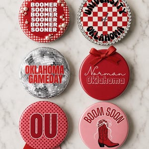 May include: Six circular decorative pins featuring University of Oklahoma themes. Designs include red gingham with pearls, a rhinestone-bordered checkerboard, a silver disco ball, a red pin with a bow, a polka-dot pin with ribbons, and a pink boot graphic.