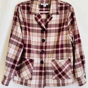 May include: A Pendleton plaid blazer in shades of burgundy, beige, and cream, with a classic button-up front and two front pockets. The blazer is hanging on a pink hanger against a white background. The Pendleton logo is visible on the collar.