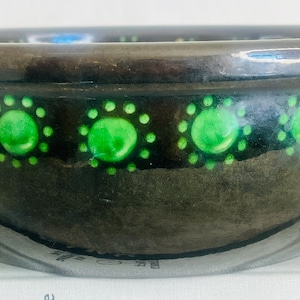May include: A black ceramic bowl with a green and white design. The bowl has a rim with a green and white pattern. The bowl is sitting on a white surface.