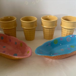 May include: A collection of ceramic ice cream cone-shaped cups and oval serving dishes. The cups are yellow with a waffle cone texture. The serving dishes are pink and blue with colourful polka dots and a waffle cone texture.