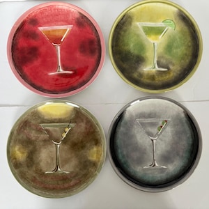 Op de afbeelding: Vier ronde decoratieve borden met cocktailontwerpen. Elk bord toont een andere cocktail in een martiniglas. De achtergronden zijn rood, groen, geel en grijs. Perfect voor een bar of keuken.