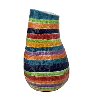 May include: A colorful ceramic vase with horizontal stripes in shades of blue, green, orange, red, purple, and yellow. The vase has a unique, slightly asymmetrical shape and a textured surface, perfect for home decor.