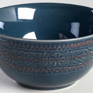 Op de afbeelding: Een teal keramische kom met een decoratief patroon aan de buitenkant. Het patroon heeft geometrische vormen en bloemelementen in een contrasterende bruine kleur. De kom heeft een glanzende afwerking.