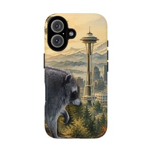 Könnte beinhalten: Eine Smartphone-Hülle mit einer Illustration im Aquarellstil, die einen Waschbären im Vordergrund zeigt. Der Hintergrund zeigt die Seattle Space Needle, Stadtgebäude, Nadelbäume und ferne Berge unter einem Himmel in warmen Farbtönen.