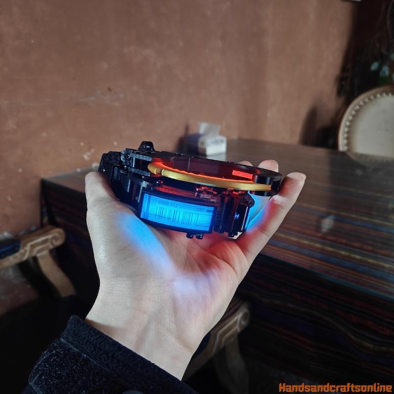 Puede incluir: Un dispositivo electr&oacute;nico negro y rojo con una pantalla azul iluminada se sostiene en una mano. El dispositivo tiene un acento dorado y una forma rectangular. La pantalla muestra una serie de l&iacute;neas verticales y n&uacute;meros. El dispositivo es probablemente una pieza de tecnolog&iacute;a o un gadget.